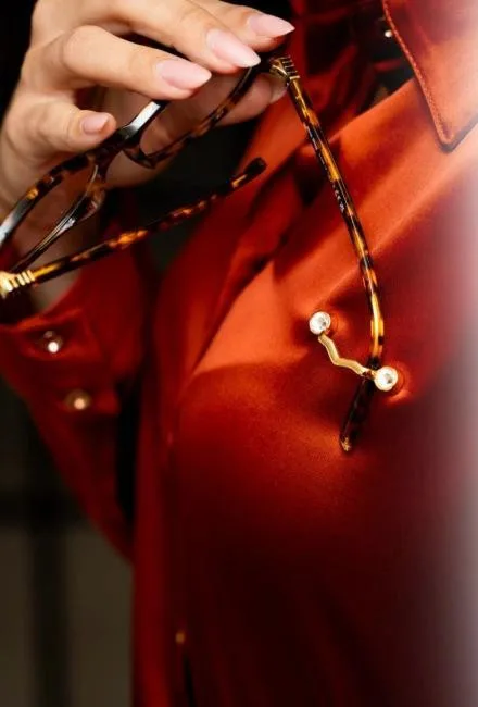 Gold MagTag Lux holding glasses on a red silk shirt